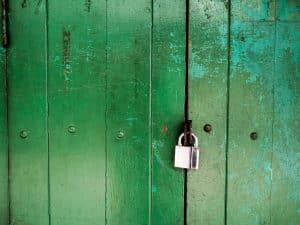 Une porte en bois vert patinée, dont la peinture s'écaille, est fermée par un cadenas argenté fixé en son centre.